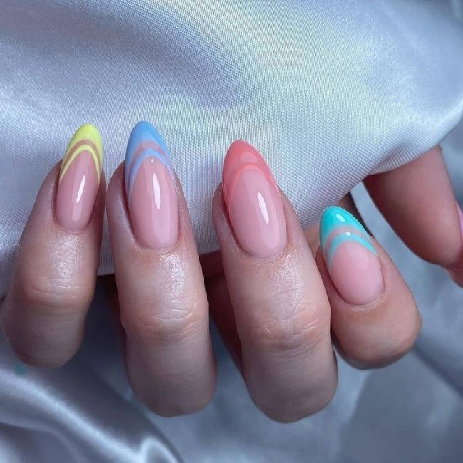 Foto mostrando uma mão com os dedos dobrados para evidenciar as unhas pintadas em francesinha colorida nas cores azul, amarelo, bege e azul mais claro.