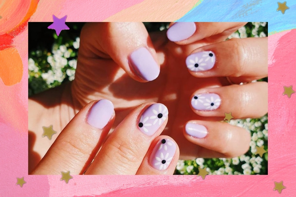 Mãos exibindo as unhas com nail art de florzinha branca com bolinha preta em fundo lilás.
