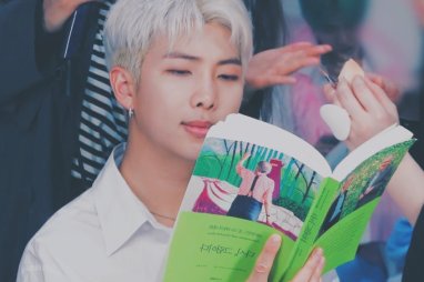 RMT lendo livro; ele usa uma camisa branca e seu cabelo está platinado, o cantor sorri levemente