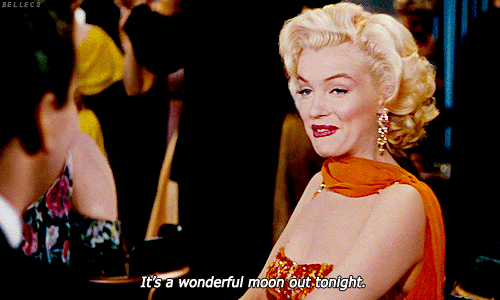 Marilyn Monroe com um vestido laranja falando para a amiga que a Lua está linda lá fora
