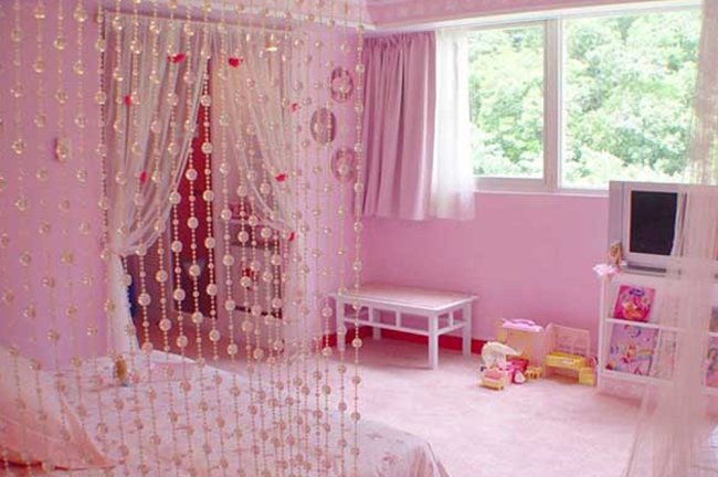 Quarto teen todo rosa com uma cortininha de miçangas ao lado da cama
