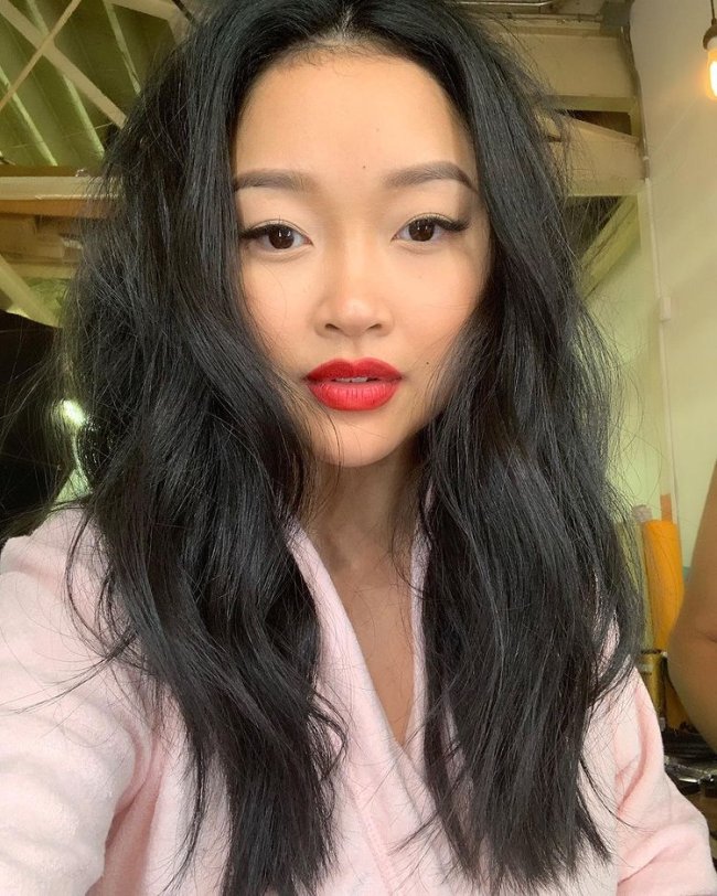 Selfie da atriz Lana Condor. Ela usa um roupão rosa, cabelo solto e make com batom vermelho. Ela olha para a câmera e não sorri.