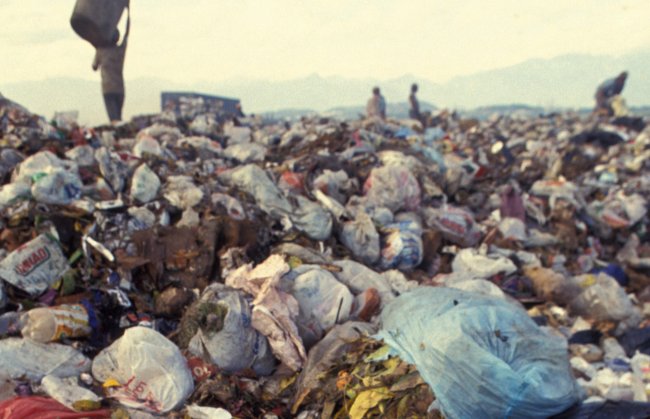 Imagem de um lixão a céu aberto; ao fundo, pessoas convivem no meio da montanha de lixo