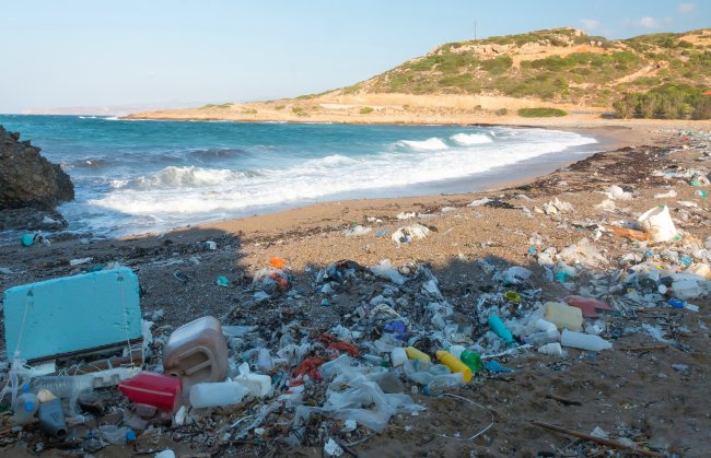 Coisas que você ainda usa, não são recicláveis e poluem o planeta por anos Imagem de uma praia cheia de lixo na areia; o mar é azul e o céu está aberto