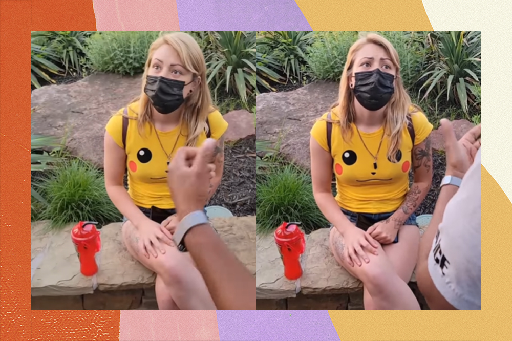 Mulher loira usando máscara de proteção preta, uma camiseta do Pikachu e um short jeans escutando ofensas de um policial. Ela está em um parque.