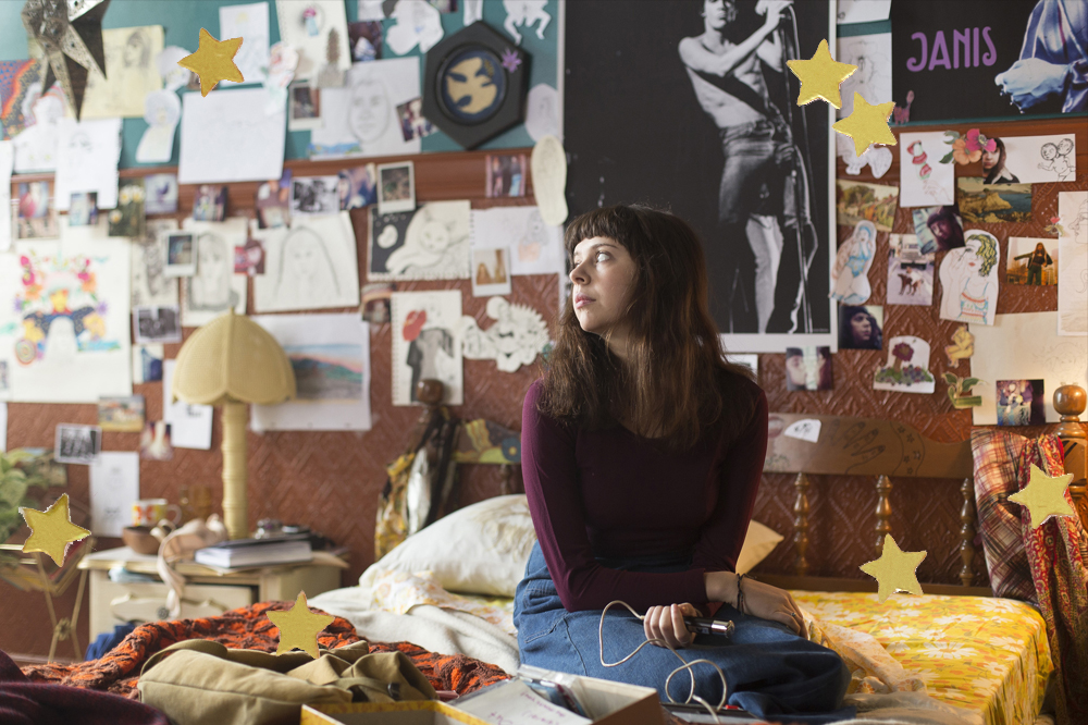 Adolescente descansa sentada na cama do quarto; a parede ao fundo é todinha repleta de pôsteres, desenhos e adesivos