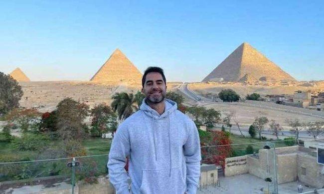 Na imagem, o médico Victor Sorrentino aparece sorrindo e usando um moletom cinza, durante viagem ao Egito. No fundo, estão duas pirâmides