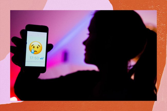 Mulher de perfil, mas com a imagem desfocada, segurando um celular. Na tela, é possível ver um emoji chorando que foi enviado pelo WhatsApp
