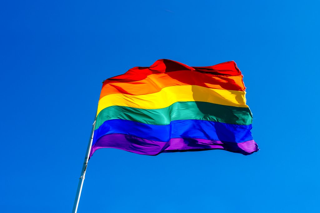 Bandeira LGBTQIA+ hasteada, e ao fundo, céu azul