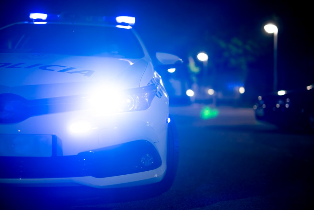 Imagem que mostra uma viatura de polícia com as luzes ligadas em uma rua à noite