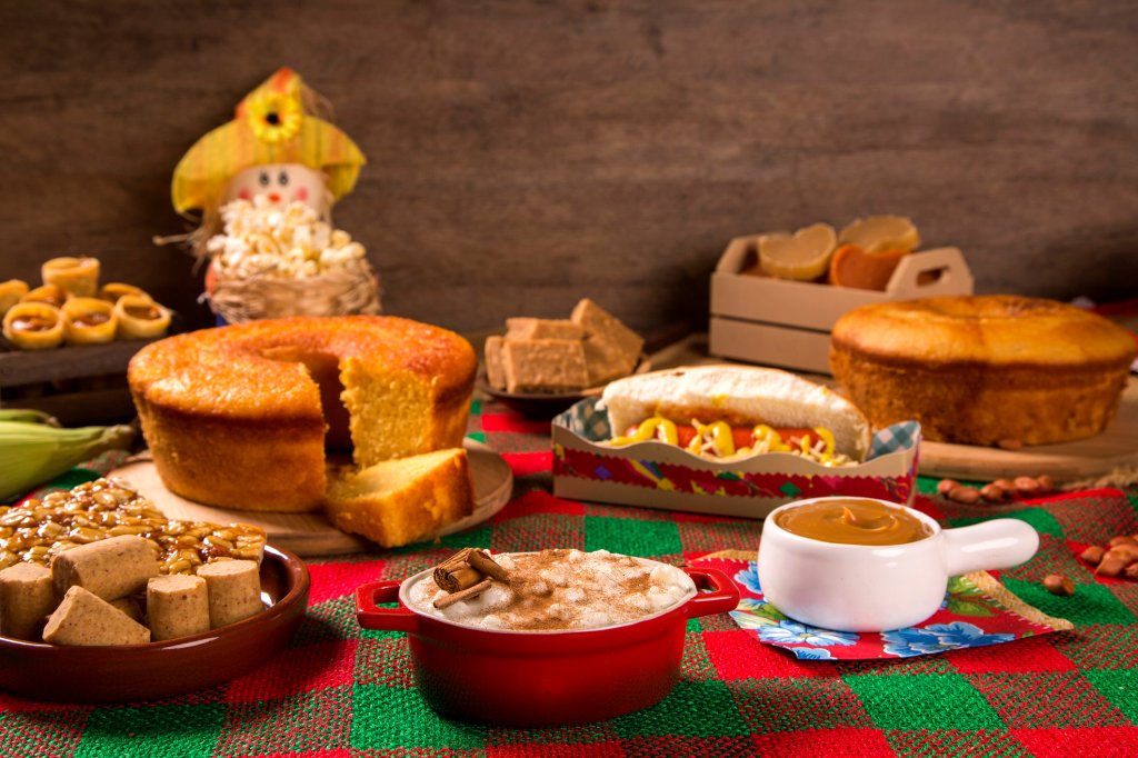 Mesa com comidas típicas juninas, como bolo de milho, cachorro-quente, arroz doce e paçoca