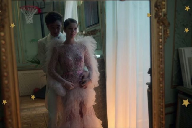 Vestido Caye Elite Personagens do seriado Elite, posando frente a espelho, abraçados, com expressão pensativa. Cayetana veste vestido delicado em camadas com detalhes em branco e rosa.
