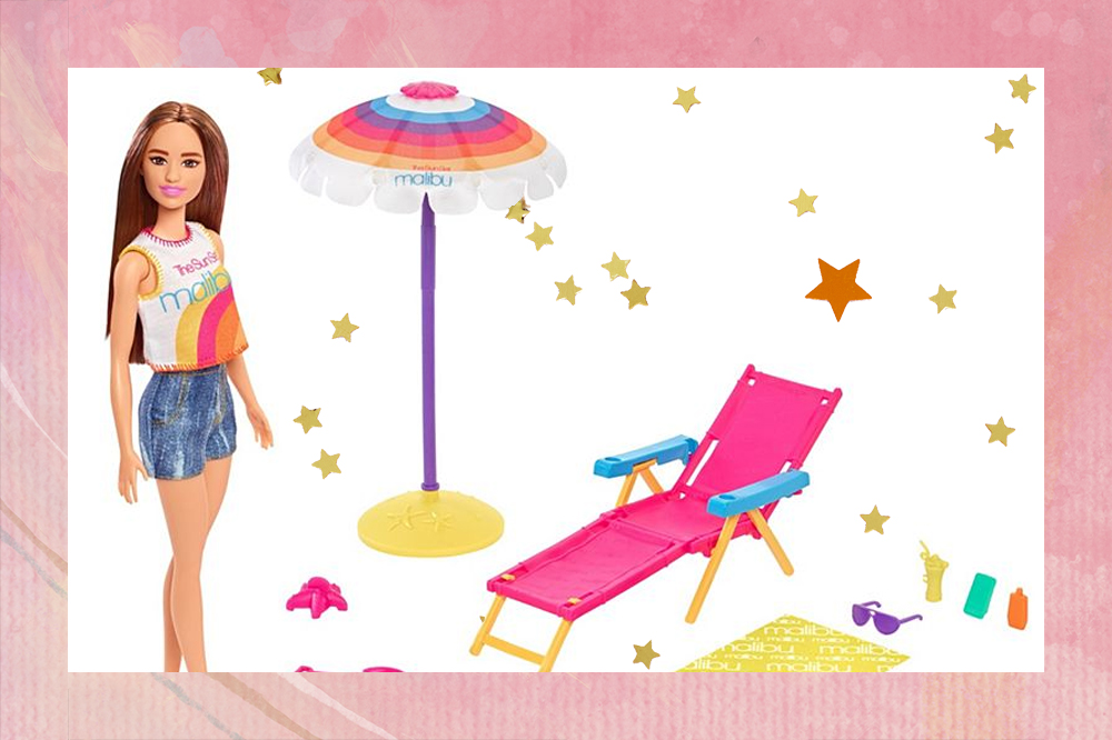 Foto de uma Barbie com roupa de praia ao lado de uma espreguiçadeira, um guarda-sol e outros itens de praia, como baldinho de areia
