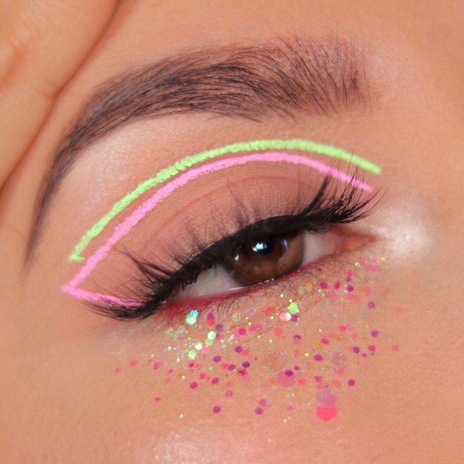 Foto de um olho. Ele está com um delineado gráfico nos tons verde e rosa pastel, com glitter na parte inferior e cílios postiço.