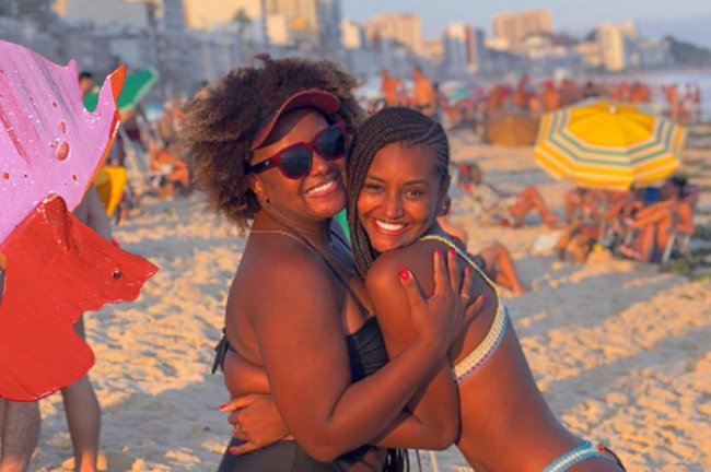 Kathlen Romeu com a mãe, Jaqueline. Elas estão abraçadas na praia, em um dia de sol.