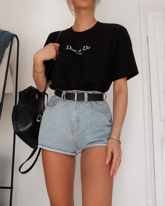 acessórios como o cinto preto transformam o look Foto do look de uma mulher. Ela usa camiseta preta, short jeans com cinto preto e mochila preta.
