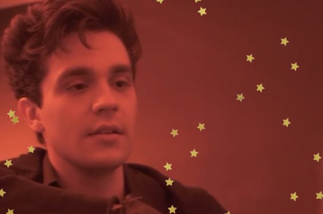 Luan Santana em prévia do clipe de Morena; ele está olhando para frente com expressão neutra e a luz do ambiente é vermelha; estrelas amarelas decoram a imagem