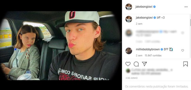 Millie Bobby Brown sentada no banco do passageiro de um carro, olha para a câmera com o queixo sobre o ombro. No banco do passageiro, Jake, usando boné, faz bico para a câmera