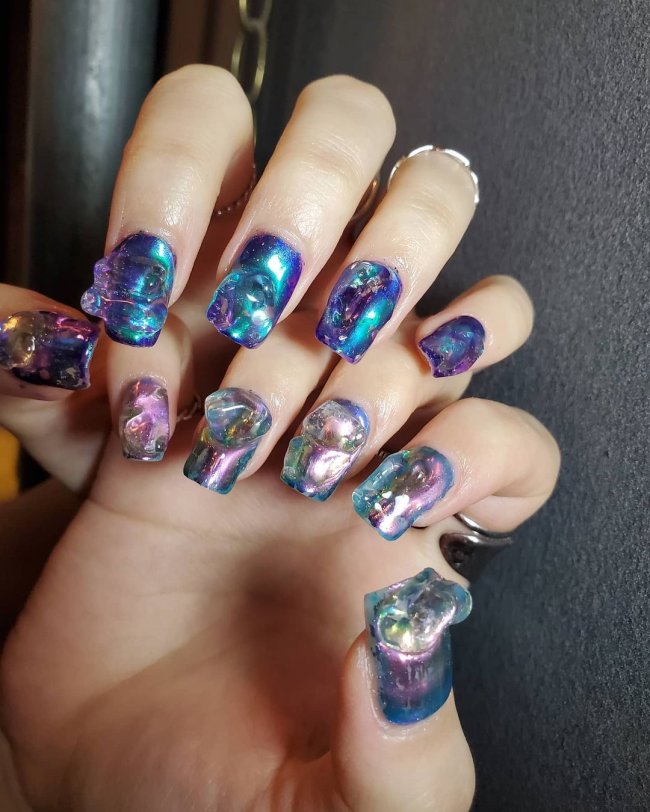 Foto com foco nas unhas de duas mãos, com gel e azul claro e escuro. Com glitter.