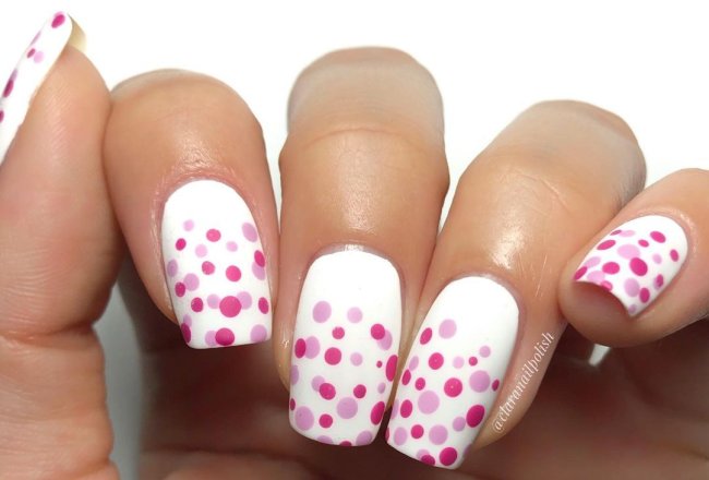 Foto com destaque nas unhas com nail art de bolinha, dessa vez com fundo branco e bolinhas em vários tons de rosa.