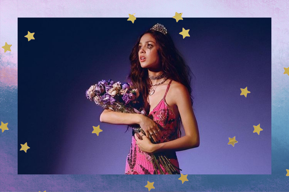 Olivia Rodrigo usando um coroa, um vestido rosa e segurando um buque de flores. Ela olha para o lado e está com a maquiagem borrada e uma cara de choro