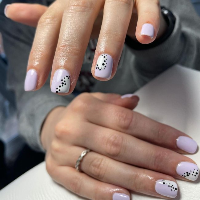 Foto com destaque nas unhas com nail art de bolinha, dessa vez com fundo lilás e bolinhas pretas.