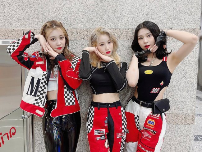 3YE_reproducao_twitter Meninas do grupo 3YE posando em uma parede neutra com roupas pretas e vermelhas; elas estão com as mãos juntas e encostadas no rosto; as três tem expressões neutras