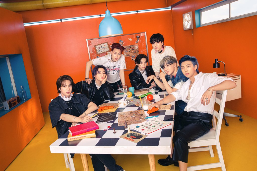 Integrantes do BTS em uma foto de divulgação sentados em uma mesa com livros, jogo de xadrez e copos. Eles olham para a câmera e não sorriem.