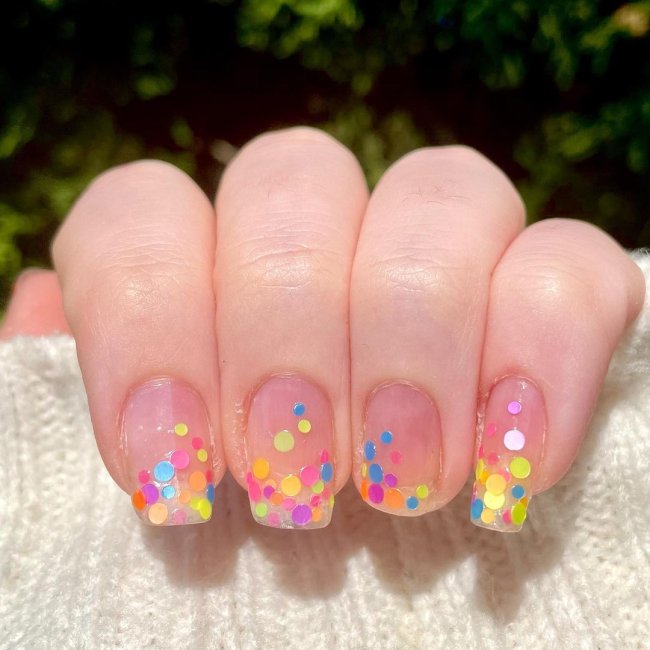 Foto com close nas unhas e tem nail art com bolinhas coloridas nas cores, azul, verde, rosa, amarelo.