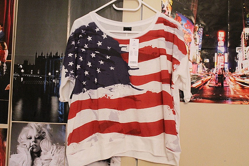 Foto de uma camiseta com estampa dos Estados Unidos pendurada em um cabide na parede de um quarto.
