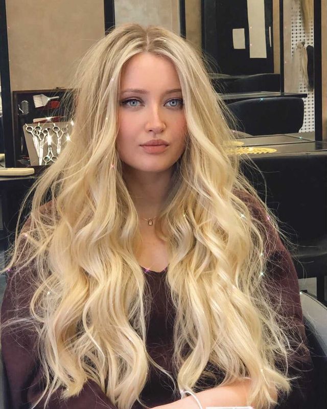 corte em camadas cabelo loiro Jovem com expressão séria sentada com cabelo loiro e longo e blusa marrom.