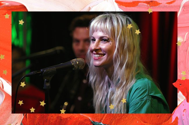 Hayley Williams aparece sorrindo, de perfil, usando camiseta verde e com os cabelos platinados, com uma franja
