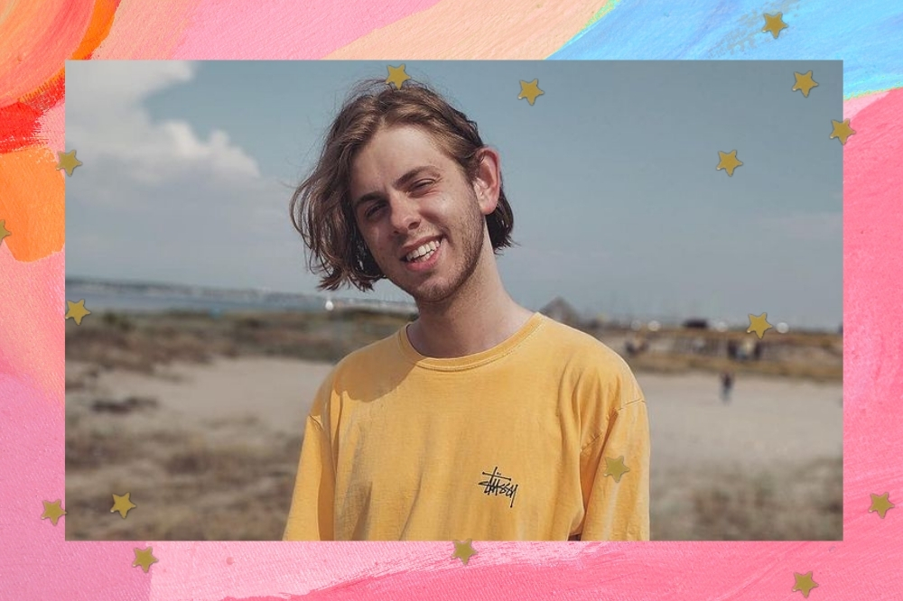 Jovem sorridente posando com camiseta amarela em praia.