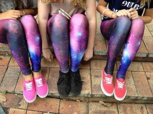 Foto da perna de três meninas sentadas em uma escada. Todas usam o mesmo modelo de calça legging com estampa de galaxia e tênis.