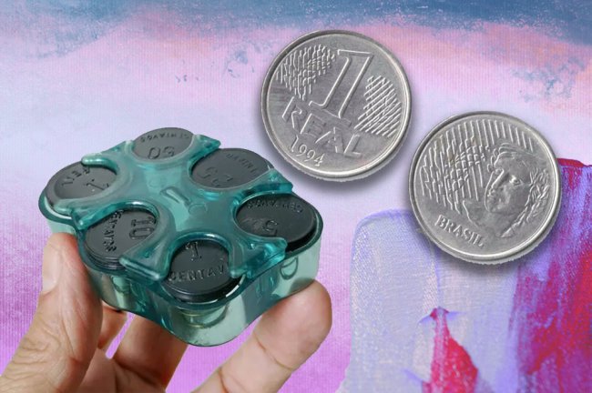 Coisas que a Geração Alpha nunca vai entender ou ter o prazer de fazer Foto de um porta-moedas de moda automático, hit dos anos 90, na cor verde. Ao lado, uma moeda de um real.