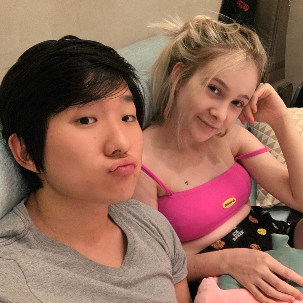 Selfie de Pyong e Sammy; ele usa uma camiseta cinza e está fazendo biquinho enquanto ela usa um top rosa e sorri levemente com a cabeça apoiada na mão