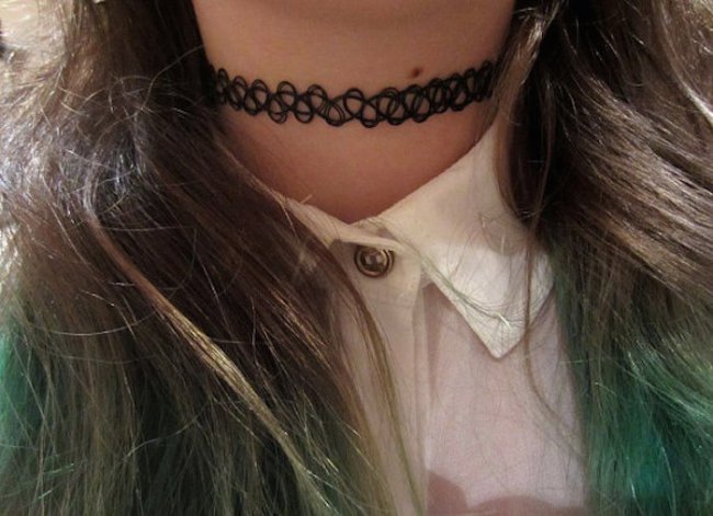 Foto do pescoço de uma menina. Ela usa uma gargantilha que imita uma tatuagem.
