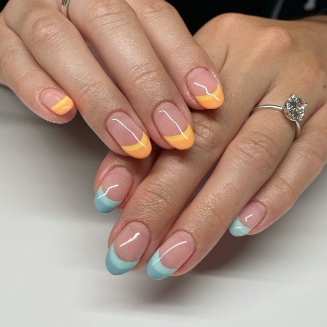 Foto com close nas unhas e tem nail art com francesinha colorida laranja e azul.
