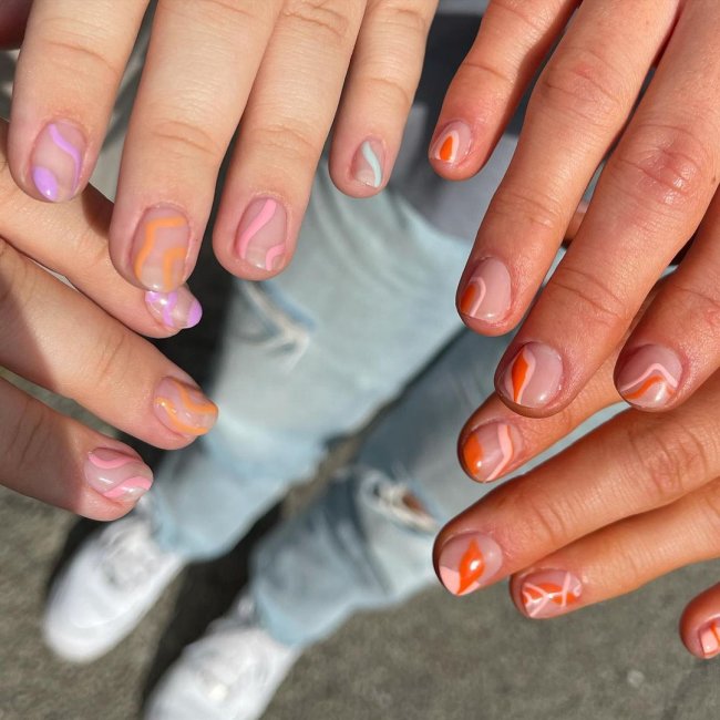 Foto com close nas unhas e tem nail art com as cores laranja, verde e lilás.