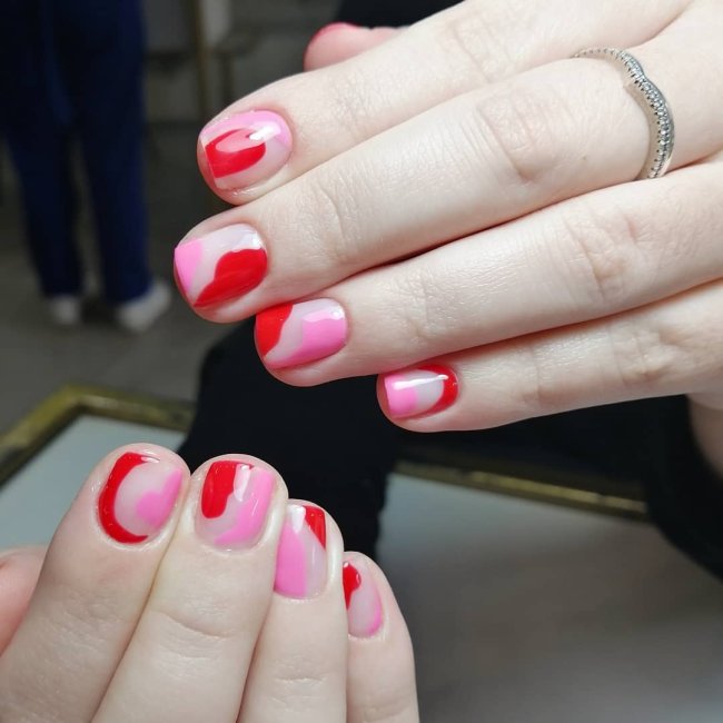 Foto com foco nas mãos mostrando nail art rosa com detalhes vermelhos.