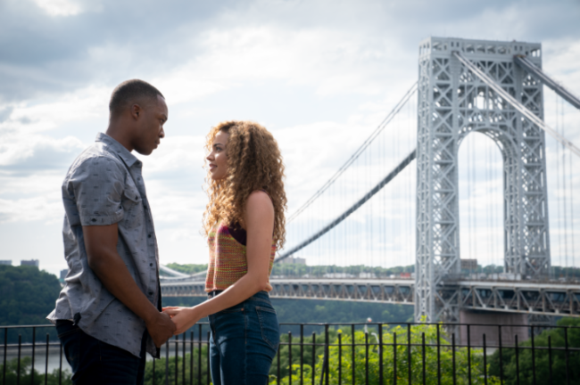 Um homem segurando as mãos de uma mulher. Ao fundo a ponte em Nova York
