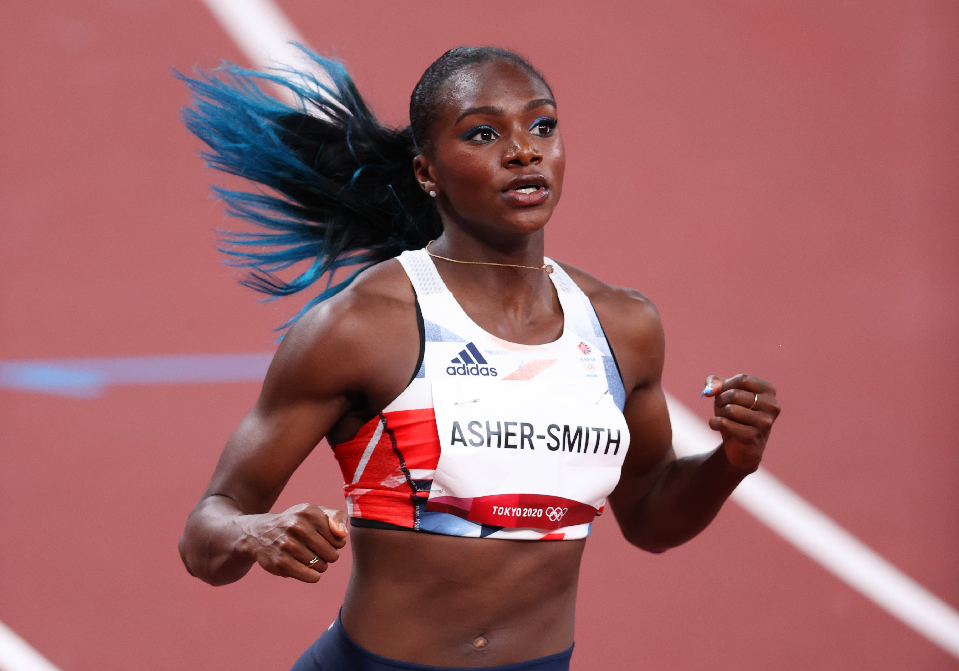 A velocista Dina Asher-Smith, da Grã Bretanha, nas Olimpíadas de Tóquio. Ela está com um top branco, cabelo amarrado em um rabo, enquanto corre na pista de atletismo.