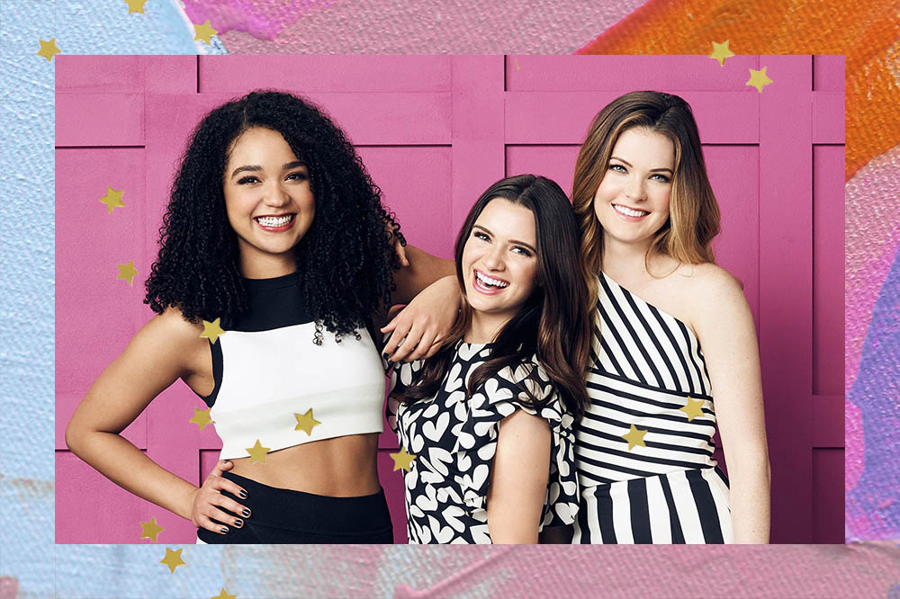 Imagem das protagonistas de The Bold Type (Kat, Jane e Sutton) em frente de parede rosa.