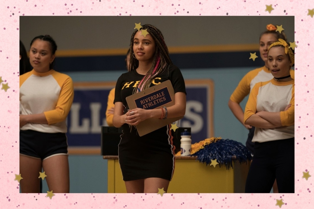 Foto da série Riverdale, com foco na personagem Toni Topaz, que usa roupa preta e segura prancheta no meio de uma quadra.