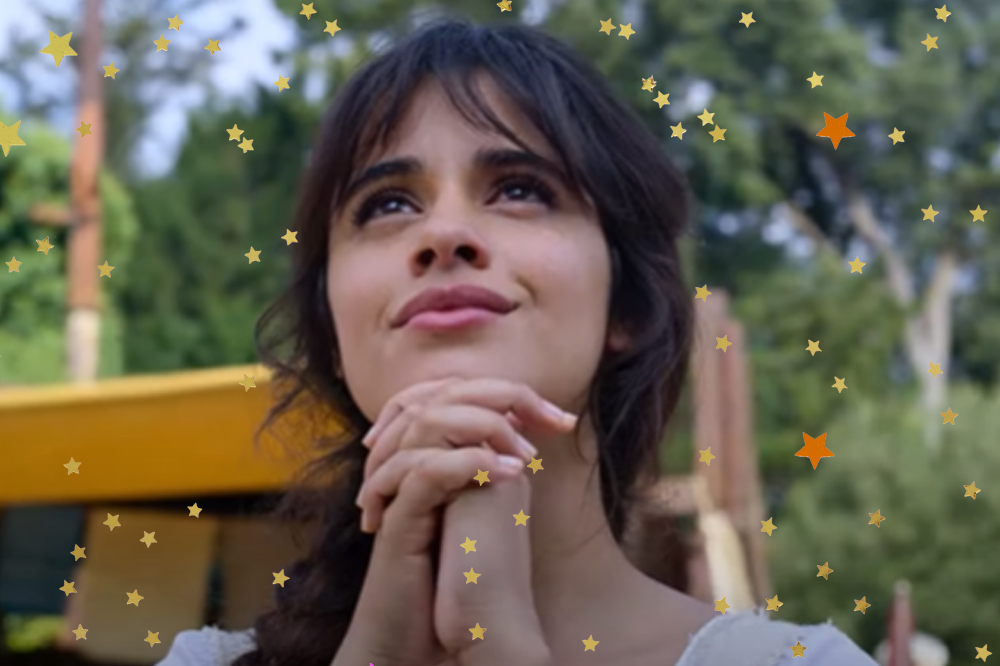 Camila Cabello em cena de Cinderela; ela está olhando para frente com o olhar sonhador e as mãos juntas na frente do rosto e encostadas no queixo com leve sorriso no rosto