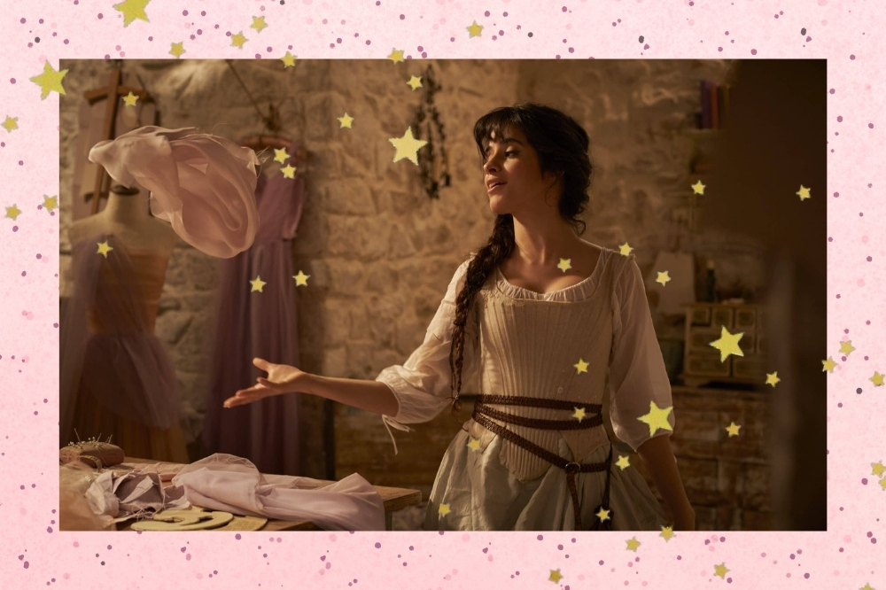 Camila Cabello em uma cena do filme Cinderella. Ela está em um quarto, usando um vestido em tons de bege com manga bufante e cabelo preso em uma trança lateral. Ela olha par o lado e está a mão direita esticada.