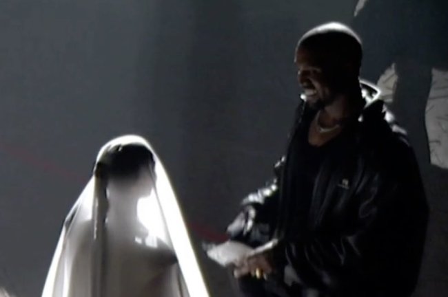 Kim Kardashian de costas com vestido e véu branco de noiva e Kanye West sorrindo para ela