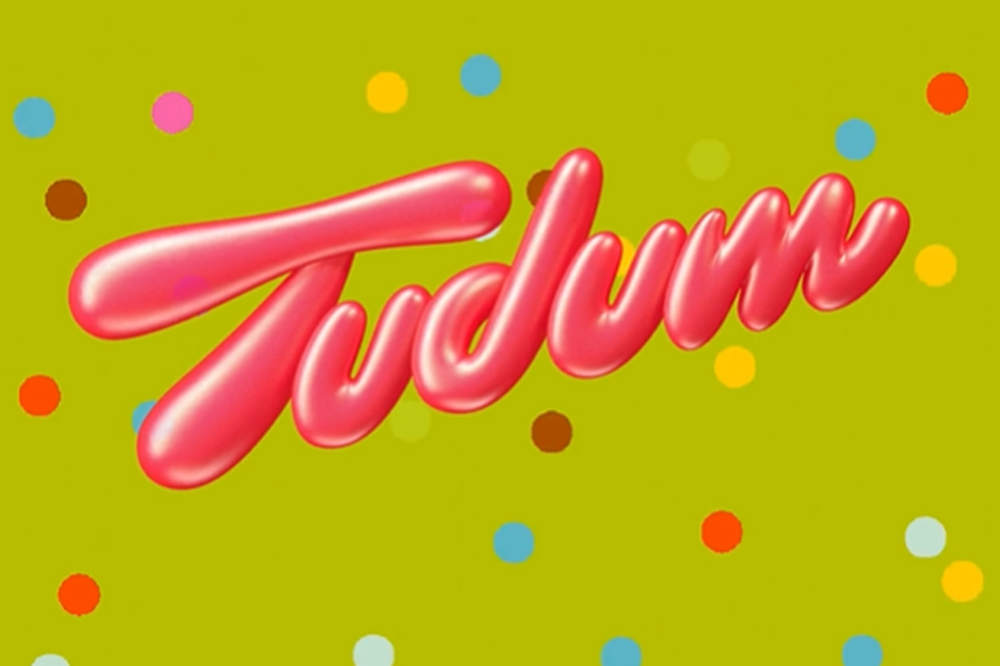 Logo do TUDUM escrito em letras garrafais rosa em um fundo verde com bolinhas coloridas