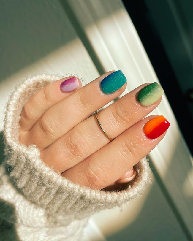 Foto com close nas unhas com esmaltes coloridos em diversas cores.