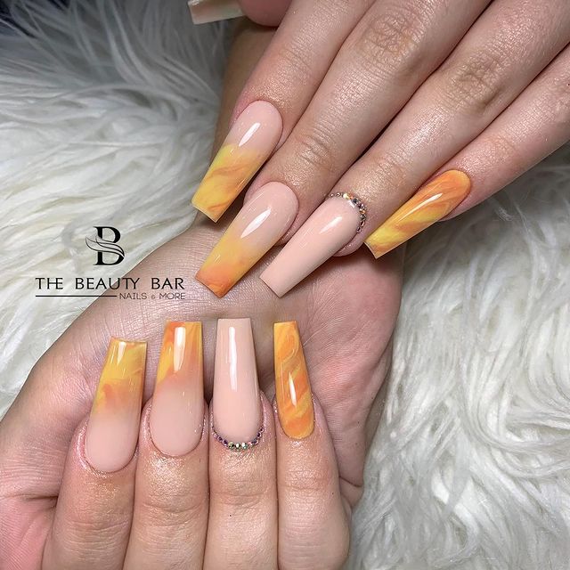 Foto de duas mãos com detalhe nas unhas decoradas no estilo baby boomer em um tom de nude e laranja.